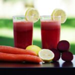 Colorful glasses of beetroot and carrot juice garnished with lemon slices, symbolizing health and freshness.