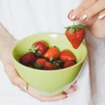 A close-up of a hand holding a green bowl filled with ripe strawberries, showcasing healthy lifestyle.