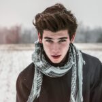 Portrait of a young man outdoors in a snowy field wearing a scarf.